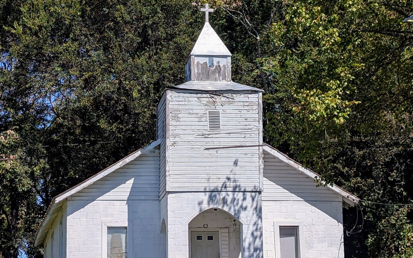 A small white country church with a steeple, surrounded by trees