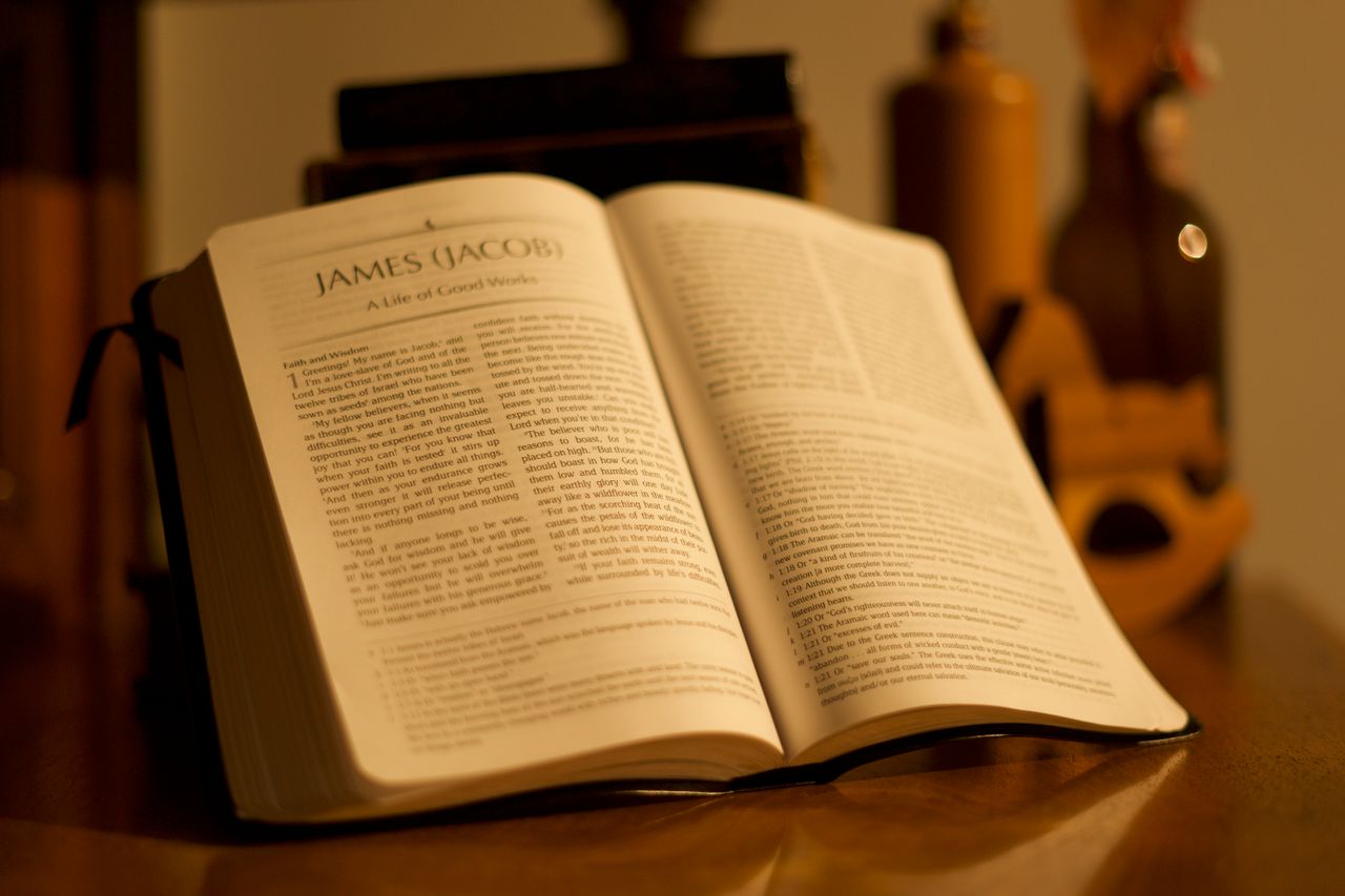 An open Bible resting on a wooden table in warm light